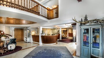Eine großzügige Empfangshalle mit Holzdetails und einem eleganten Empfangstresen. Die Gestaltung ist modern und einladend, mit einem schönen Teppich im Vordergrund.
