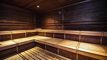 Eine Holzsauna mit hellen Bänken und sanfter Beleuchtung. Der Raum strahlt Entspannung und Wärme aus.