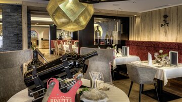 Ein elegantes Restaurant mit stilvollen Tischen und einer auffälligen Lampe. Auf dem Tisch steht eine große Flasche Wein und Dekorationen sind sorgfältig arrangiert.