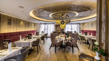 Ein elegantes Restaurant mit stilvollen Tischen und bequemen Stühlen. Die warme Holzdecke und das sanfte Licht schaffen eine einladende Atmosphäre.