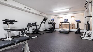 Ein modernes Fitnessstudio mit verschiedenen Trainingsgeräten. Es ist gut beleuchtet und mit Teppichboden ausgestattet.