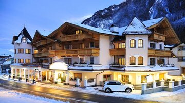 A charming hotel in winter with snow-covered streets. The facade is warmly lit, surrounded by picturesque mountains.