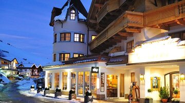 A charming hotel in the mountains, surrounded by snow. The building features rustic architecture and glows gently in the evening twilight.