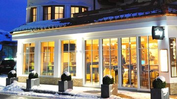 A modern restaurant with large windows in a snowy environment. It is nighttime, and the warm lights illuminate the facade.