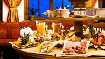 A beautifully set table with a variety of foods and drinks. There is bread, cold cuts, fruit, and juices.