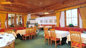 An inviting restaurant with wooden furniture and colorful curtains. The tables are decorated and invite guests to dine.