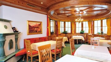 A cozy restaurant with wooden furniture and large windows. The tables are elegantly set and the walls are decorated with artworks.
