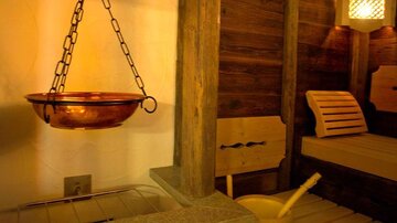 A cozy sauna area with a copper basin and wooden loungers. The warm lighting creates a relaxing atmosphere.
