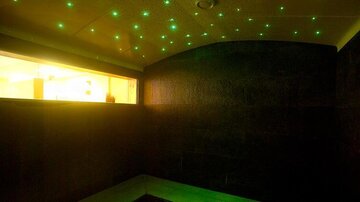 A relaxing room with dark walls and a sparkling starry sky in green lights. Soft yellow light streams through a window.
