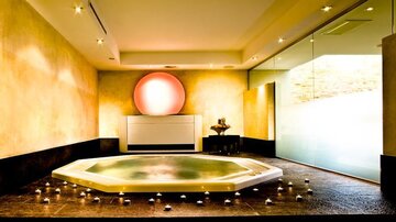 An elegant wellness area with a hexagonal whirlpool and soft lighting. The walls are in warm tones, and candles create a relaxing atmosphere.