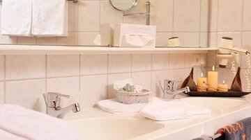 A clean bathroom with a bathtub, white towels, and a decorative tray. On the tray are candles, a small basket, and toiletries.