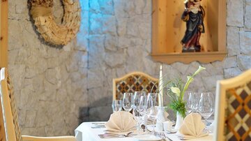 Ein elegant gedeckter Tisch in einem gemütlichen Restaurant. Im Hintergrund hängen dekorative Elemente an der Steinwand.
