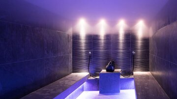 Ein moderner Wellnessbereich mit sanftem blauem Licht und eleganten Steinoberflächen. In der Mitte befindet sich ein stilvolles Wasserbecken.