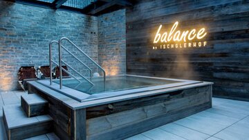 Ein moderner Wellnessbereich mit einem Whirlpool und Holzverkleidung. Die Wand ist mit der leuchtenden Schrift „balance by Ischglerhof“ gestaltet.