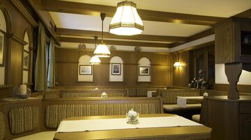 Ein gemütliches Restaurant mit Holzverkleidung und stilvollen Lampen. Tische sind mit weißen Tischdecken und Blumen dekoriert.