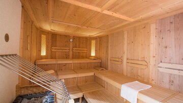 Eine warme Sauna mit Holzbank und Steinofen. Sanftes Licht fällt durch die Fenster und schafft eine entspannende Atmosphäre.