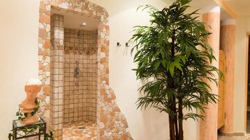 Ein eleganter Duschbereich mit Natursteinfliesen und einer grünen Pflanze. Der Raum strahlt eine entspannende Atmosphäre aus.