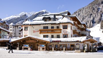 A charming hotel in the snow, surrounded by mountainous landscapes. The buildings have wooden facades and are nestled in an idyllic winter landscape.