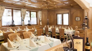 A rustic restaurant with wooden walls and elegant tables. The tables are festively set and invite a cozy meal.