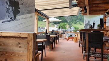 Ein gemütliches Restaurant mit Holzdekor und einem Blick auf grüne Berge. Die Terrasse ist einladend und bietet Platz für Gäste.