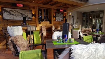 Ein gemütliches Restaurant mit Holzdekor und modernen Möbeln. Die Tische sind mit bunten Tischdecken und Dekorationen geschmückt.