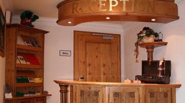 Eine gemütliche Hotelrezeption aus Holz mit einem Empfangstresen. Im Hintergrund befindet sich ein Regal mit Informationsmaterialien.
