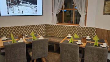 Ein modernes Restaurant mit gemütlichen Sitzplätzen und Tischen. An der Wand hängt ein Bildschirm, der ein Bild zeigt.