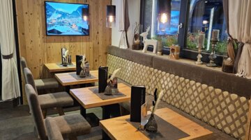 Ein gemütliches Restaurant mit Holztischen und gepolsterten Sitzbänken. An der Wand hängt ein Fernseher, und die Atmosphäre ist warm und einladend.