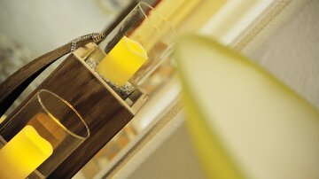 Eine dekorative Kerzenhalterung mit gelben Kerzen in Glasbehältern. Im Hintergrund sind unscharfe Farben zu sehen, die ein gemütliches Ambiente schaffen.