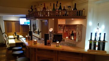 Eine gemütliche Bar mit einer Holztheke und einer Auswahl an Getränken. Im Hintergrund sind Sitze und ein Fernseher sichtbar.